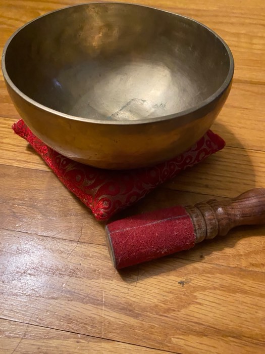 A Tibetan singing bowl resting on a red cushion with its wooden mallet